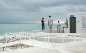 Three People Standing on White Surface Near Body of Water